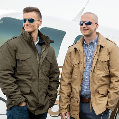 two people wearing flight jackets in front of plane